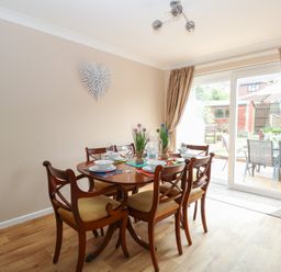 A dining area with wooden table and chairs set for six with wall decoration and sliding glass door to a garden at White Lion Retreat in Cromer