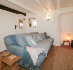 A living room with a sofa pillows blanket side table lamp and a rug at 3 Cumberland Cottages in Ringmore