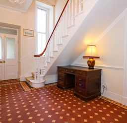 An entryway with a wooden desk and lamp under a staircase with white balusters and a patterned tile floor at Fir Grove in Menai Bridge