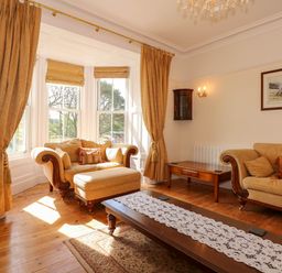 A living room with beige sofas a large window with curtains and a wooden coffee table at Fir Grove in Menai Bridge