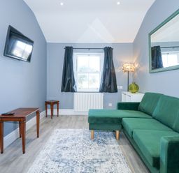 A living room with a green sofa a wall-mounted tv a window with black curtains and a patterned rug at The Fir Grove Annex in Menai Bridge