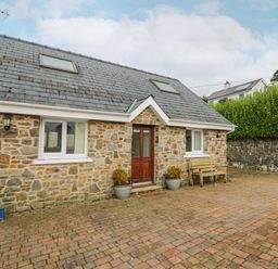 A stone house with a wooden door two windows a bench and potted plants on a paved driveway at Trevone in Goodwick