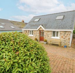 A stone house with a slate roof two windows and a wooden bench on a brick driveway with a green bush in front at Trevone in Goodwick