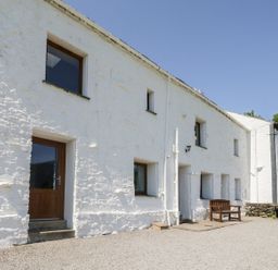 White stone building with multiple windows and doors and a wooden bench outside at Bramble Cottage in Thornthwaite near Braithwaite