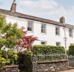 Row of white terraced houses with chimneys in front of stone wall and green hedges at Middletown in Keswick