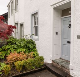 An exterior view of a white house with a blue door and various plants including a red-leaved tree at Middletown in Keswick