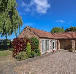 A brick house with tiled roof and large windows surrounded by plants and a gravel driveway at Providence Court Near Easingwold