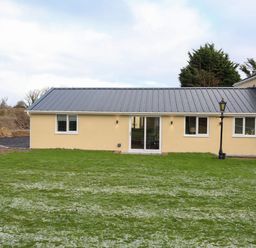 A single story building with a metal roof and several windows on a grassy lawn with a lamp post near Ynys Uchaf Near Benllech