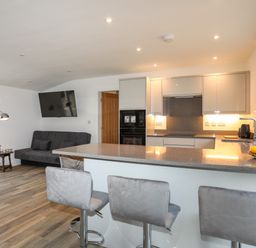 A modern kitchen with gray bar stools a sofa and a television mounted on the wall at Ynys Uchaf Near Benllech