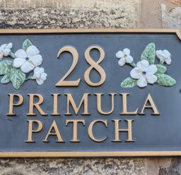 A house number plaque with the number 28 and the words Primula Patch with flower decorations at Primula Patch in Akeld near Wooler