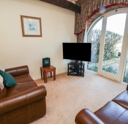 A sitting room with two brown leather sofas a small wooden table and a television by glass doors at Primula Patch in Akeld near Wooler