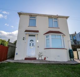 A two-story house with a front door and bay window with a lawn and fences at Hilltop Cottage in Paignton