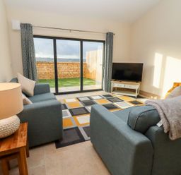 A living room with two blue sofas a lamp on a wooden side table a television on a white stand and sliding glass doors leading outside at Bears Court Barn 1 Little Rissington near Bourton-On-The-Water