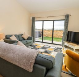A living room with sofas a TV on a stand and sliding glass doors at Bears Court Barn 1 Little Rissington near Bourton-On-The-Water