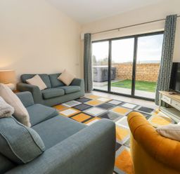 A living room with sofas a lamp rug and TV with sliding glass door at Bears Court Barn 1 Little Rissington near Bourton-On-The-Water