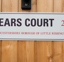 A sign on a wooden wall showing Bears Court 2 Gloucestershire Borough of Little Rissington