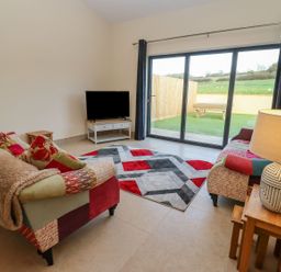 A living room with two patterned sofas a patterned rug a TV on a stand and sliding glass doors leading to a garden at Bears Court Barn 2 Little Rissington near Bourton-On-The-Water