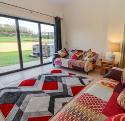 A living room with patchwork sofas a geometric rug and sliding glass doors opening to a garden at Bears Court Barn 2 Little Rissington near Bourton-On-The-Water