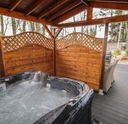 An outdoor hot tub with wooden privacy panels and a covered roof beside a wicker chair on a deck at Drumrane Lodge in Dungiven Londonderry