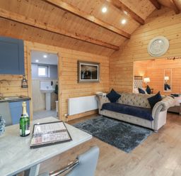 A wooden room with a blue sofa a gray rug blue kitchen cabinets a table with a bottle and flowers and a bed visible in the next room at Drumrane Lodge in Dungiven Londonderry