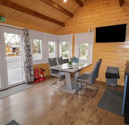 A dining area with a table and four chairs next to windows and a wall-mounted TV at Drumrane Lodge in Dungiven Londonderry
