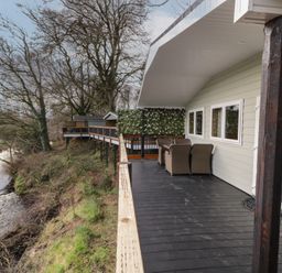 A wooden deck with outdoor chairs beside a river at Railway Lodge in Dungiven Londonderry
