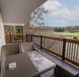 A balcony with wicker chairs and a table overlooking fields and trees at Railway Lodge in Dungiven Londonderry