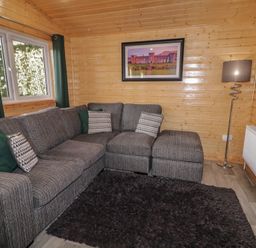 A living room with a gray sectional sofa green and patterned cushions a floor lamp a wall-mounted TV and a framed picture at Railway Lodge in Dungiven Londonderry