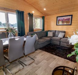 A wooden living room with a grey corner sofa white dining table and grey chairs at Railway Lodge in Dungiven Londonderry