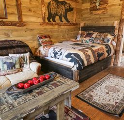 A rustic bedroom with a wooden bed and nature-themed bedding a wooden coffee table with red apples on it a cream sofa with bear and cabin cushions at Bear Claw Lodge in Castlerock