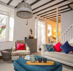 A living room with floral armchair red and blue cushions on a gray sofa wooden beams on ceiling at Riverwash Cottage in Dwygyfylchi