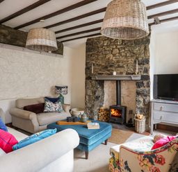 A living room with a stone fireplace a wood stove sofas with colorful cushions an ottoman and a TV on a cabinet at Riverwash Cottage in Dwygyfylchi