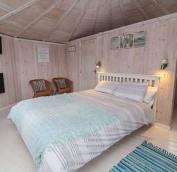 A bedroom with a double bed two chairs a wall mounted TV and fireplace at Shipload Bay near Hartland