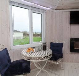 A small dining area with two cushioned chairs and a round table with cups and croissants near a window and a wall-mounted TV at Shipload Bay near Hartland