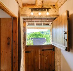 An open stable door with wooden beams and window shutters showing a green landscape outside at Upper Cottage in Rocombe near Uplyme