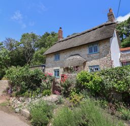 A cottage with a thatched roof surrounded by a garden at Upper Cottage in Rocombe near Uplyme