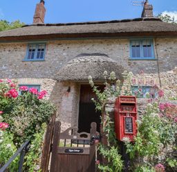 A cottage with thatch roof and flower bushes at Upper Cottage in Rocombe near Uplyme