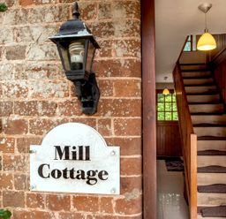 A brick wall with a lamp and Mill Cottage sign next to a wooden staircase inside a house at Mill Cottage in Aylesbeare