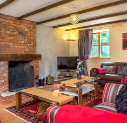 A living room with brick fireplace wooden beams glass coffee tables and striped armchair at Mill Cottage in Aylesbeare