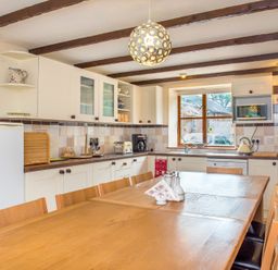 A kitchen with wooden dining table and chairs white cabinets and a refrigerator at Mill Cottage in Aylesbeare