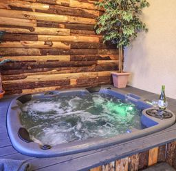 A hot tub with bubbling water beside two potted plants and a bottle of wine with two glasses at Cob Barn in Aylesbeare