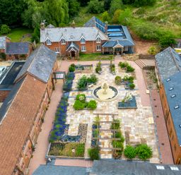 An aerial view of a courtyard with a fountain and garden beds surrounded by brick buildings at Cob Barn in Aylesbeare