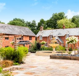 A courtyard with garden beds and a fountain in front of brick houses at Cob Barn in Aylesbeare