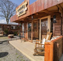 A wooden cabin exterior with a porch bench rocking chair and potted plants at Whiskey Creek Cabin in Castlerock