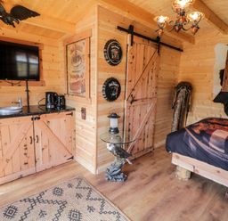 A wooden cabin room with a bed a flat screen tv a wooden cabinet a glass table with an eagle sculpture and a rusty door at Whiskey Creek Cabin in Castlerock