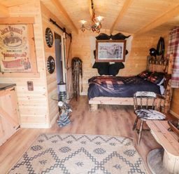 A wooden cabin interior with a bed a chair and a coffee table near a window at Whiskey Creek Cabin in Castlerock