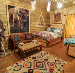 A bedroom with two beds wooden walls a wooden bench a coffee table and a statue at Apache Falls Lodge in Castlerock