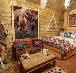 A bedroom with a bed patterned blanket wooden bench coffee table with skulls and a large native american statue at Apache Falls Lodge in Castlerock