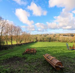 A grassy field with farm equipment and trees under a blue sky at Audrey in Penzance near Newlyn