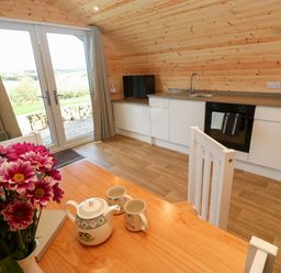 A kitchen with white cabinets and wood paneled walls near a table with a teapot cups and flowers at Audrey in Penzance near Newlyn